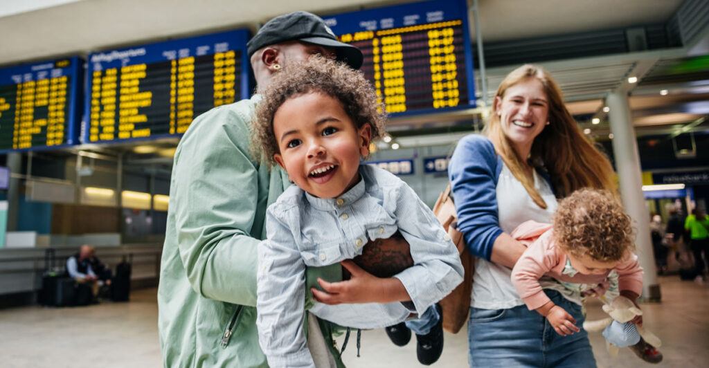 A mixed-race couple carries and swings their cute children through an airport.