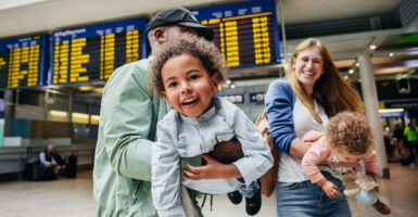 A mixed-race couple carries and swings their cute children through an airport.