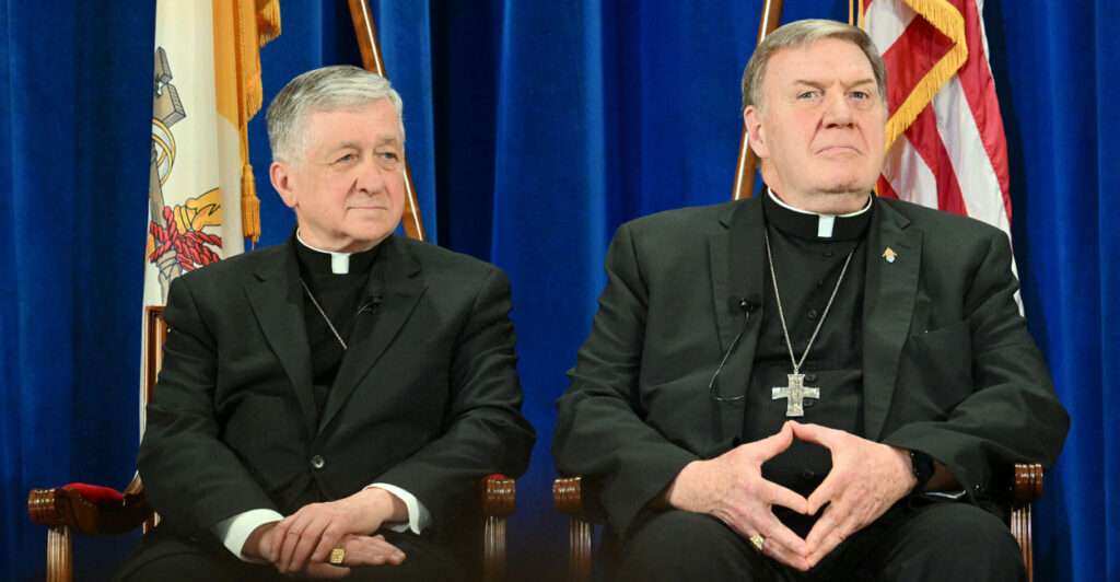 Cardinal Blase Joseph Cupich and Cardinal Joseph Tobin sit together in front of a blue curtain.