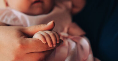 A baby girl holds her mother finger.
