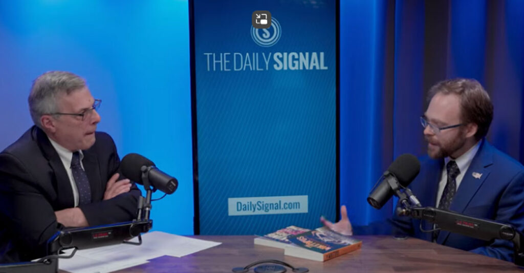 Jack Fowler and Tyler O'Neil talk at a studio table against a blue backdrop with screen reading "The Daily Signal."