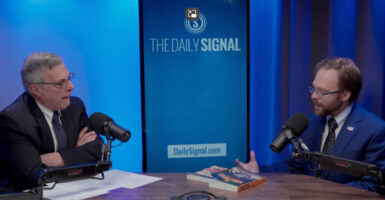 Jack Fowler and Tyler O'Neil talk at a studio table against a blue backdrop with screen reading "The Daily Signal."
