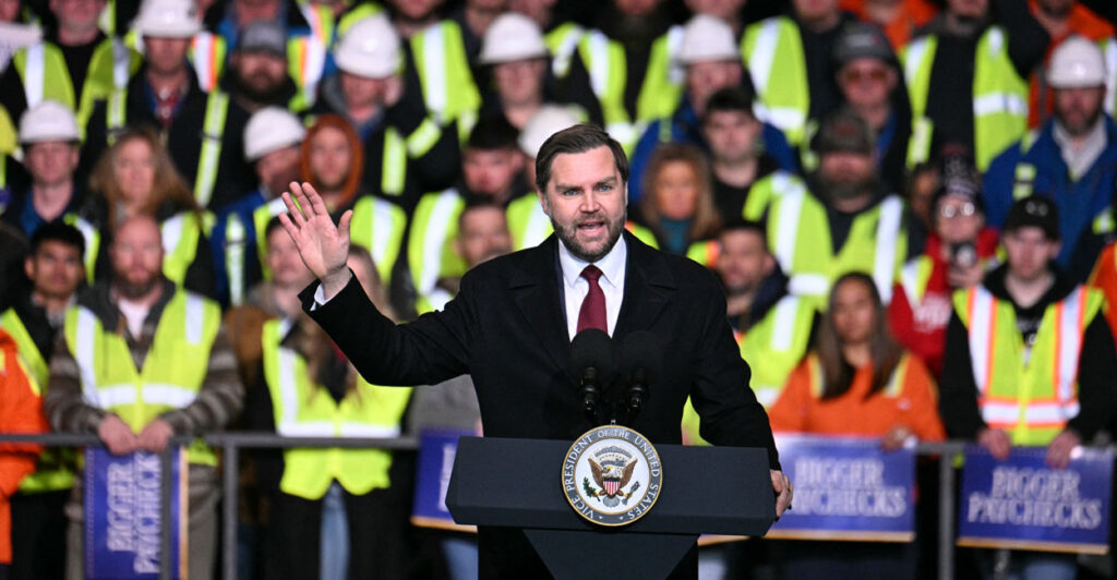 Vice President JD Vance stands at a lectern while factory members stand behind him.