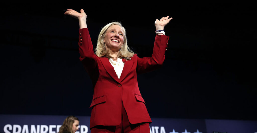 Abigail Spanberger in a red suit with her arms raised.