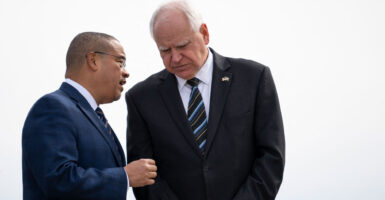 Keith Ellison speaks with Tim Walz against a white background.