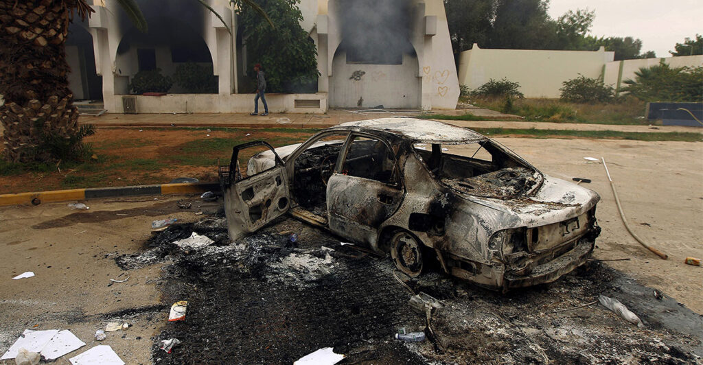TOPSHOT - The wreckage of a burnt car is seen outside a building used by Ansar al-Sharia militia after it was torched by residents on November 25, 2013 in Benghazi. Military governor Colonel Abdullah al-Saidi declared a "state of alert" after Jihadist group Ansar al-Sharia attacked Libyan special forces in Benghazi, sparking an all-out battle in which at least five soldiers died, in what was the first such confrontation between the army and Libya's top jihadist group. AFP PHOTO/ABDULLAH DOMA (Photo by ABDULLAH DOMA / AFP) (Photo by ABDULLAH DOMA/AFP via Getty Images)