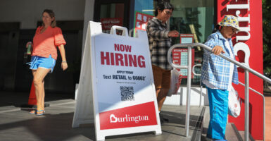Older woman, young man and woman walk around Burlington "Now Hiring" sign outside a store.