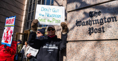A male demonstrator holds a sign reading "Don't Gut the Newsroom. Save the Post" outside the Washington Post building.
