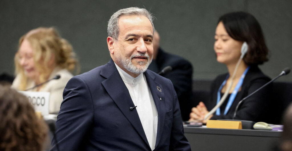 Iranian Foreign Minister Abbas Araghchi in black jacket and white shirt strolling.