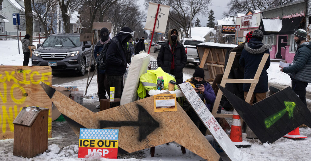 Anti-ICE protesters stand behind a makeshift barrier blocking a Minneapolis street.