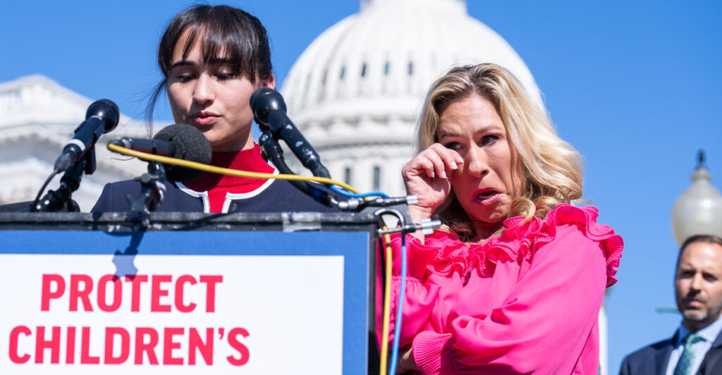 Detransition advocate Chloe Cole speaks at a podium in front of U.S. Capitol, as Marjorie Taylor Green stands behind her wiping away a tear.