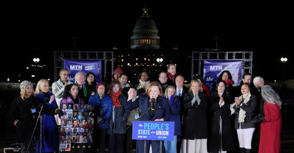 MoveOn Executive Director Katie Bethell speaks during the "People's State of the Union" at the National Mall, with a group of people and U.S. Capitol in background.