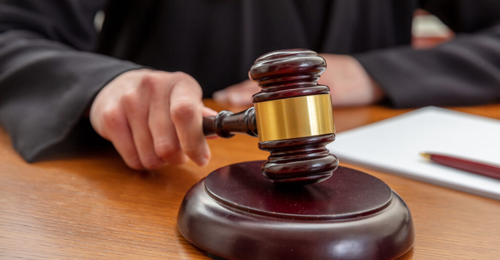 Female hand holding an auction law gavel. Woman judge with a notepad beating a wooden mallet, close up view.