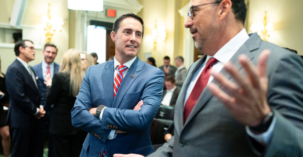 Ohio Secretary of State Frank LaRose speaks with his arms crossed to Arizona Secretary of State Adrian Fontes, who is gesturing.