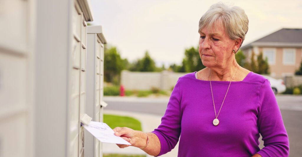 A senior age woman putting her vote by mail ballot into a mailbox.