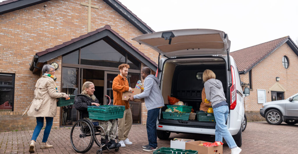 Volunteers unloading a van filled with food in trays for a food bank. They are in the North East of England. They are working together, passing the food back and forth.