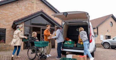 Volunteers unloading a van filled with food in trays for a food bank. They are in the North East of England. They are working together, passing the food back and forth.
