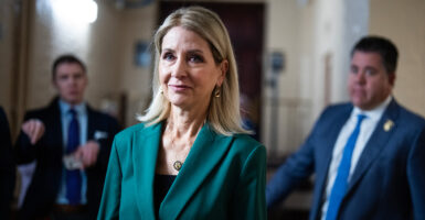 Rep. Mary Miller in green jacket walks through Capitol corridor.