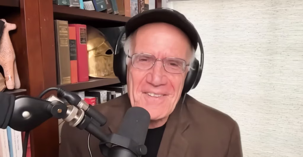 A smiling Victor Davis Hanson wearing headphones in front of a microphone.