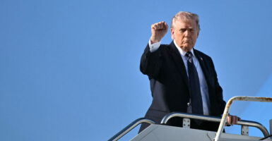 President Donald Trump raises his fist at the top of the stairs to Air Force One against a perfect blue sky.