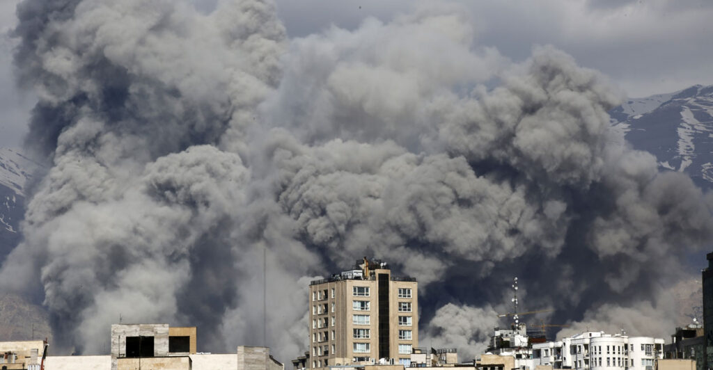 Huge dark plus of smoke rise above a row of buildings.