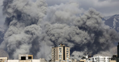 Huge dark plus of smoke rise above a row of buildings.