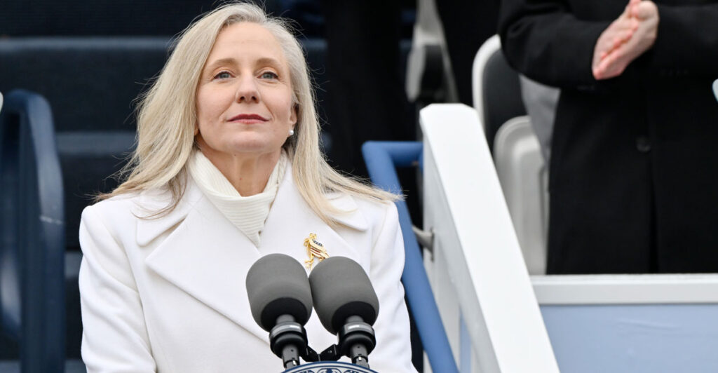 Abigal Spanberger in a white coat stands in front of microphones.