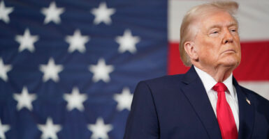 President Donald Trump looks off to his left in front of a large American flag.