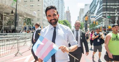 Zohran Mamdani smiling while holding an LGBT flag.