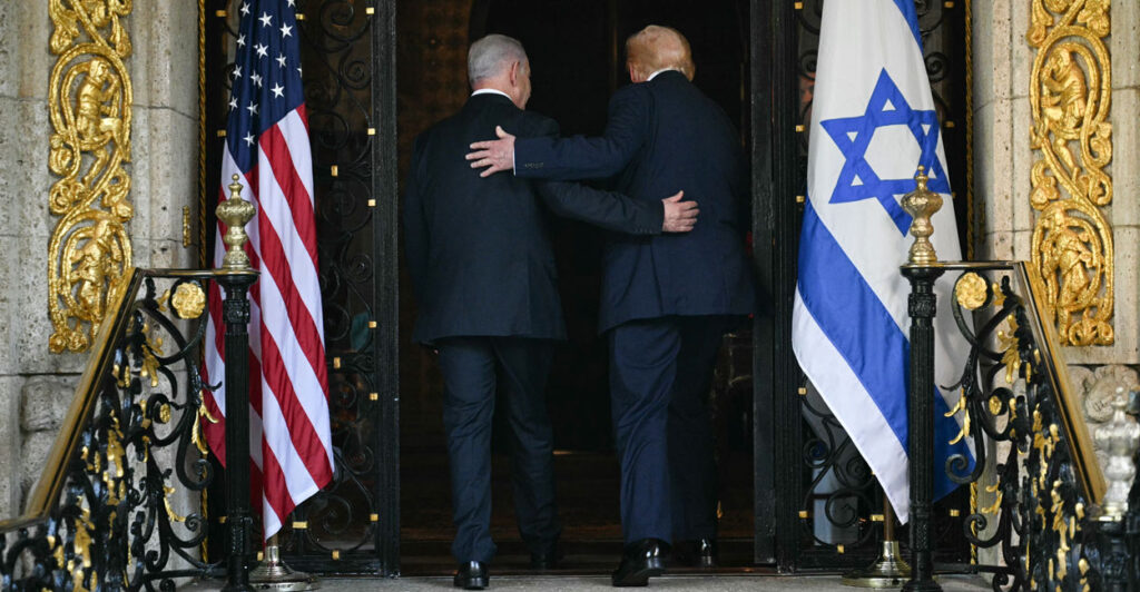 Benjamin Netanyahu and Donald Trump walk with arms on each other's back into doorway flanked by American and Israeli flags.