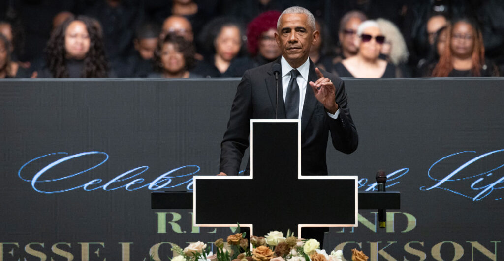 Barack Obama with his index finger on left hand pointing upward speaks behind a black cross at the funeral of Jesse Jackson.