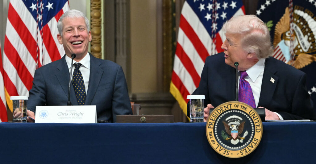 A laughing Energy Secretary Chris Wright being addressed by President Donald Trump as they sit at a long table.