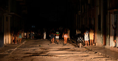 Cuban citizens on dark street lit only by car headlights amid blackout.
