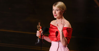 Jessie Buckley in a red top and pink dress holds her Oscar while giving her acceptance speech.