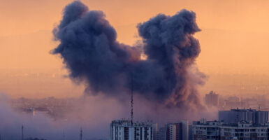Two plumes of smoke rise above Tehran against an orange sky.