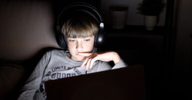 Boy in shirt reading "No Limits, No Rules" in a dark room, his face lit by a computer screen.