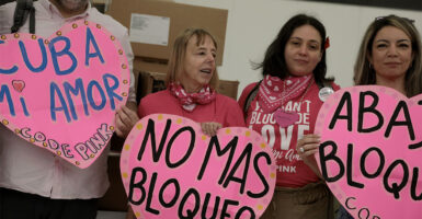 MIAMI, FLORIDA - MARCH 20: (L-R) Medea Benjamin, Jazmin Rumbaut,and Michelle Ellner from CODEPINK hold signs as they check in boxes of humanitarian aid at Invicta Air Charter in the Miami International Airport on March 20, 2026 in Miami, Florida.