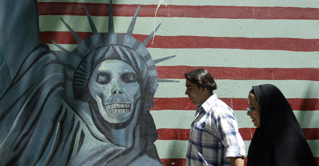 TEHRAN, IRAN: An Iranian couple walk past an anti-US mural painting outside the former United States' embassy in Tehran, 07 June 2005. Iranian voters are more accustomed to hearing their politicians chant "Death to America" -- but ahead of next week's presidential election the issue of relations with the US has been turned on its head. It is an ironic shift for the Islamic republic, founded on the dogma of resisting "Zionist-American conspiracies" and priding itself on standing up to the "Great Satan". AFP PHOTO/ATTA KENARE (Photo credit should read ATTA KENARE/AFP via Getty Images)