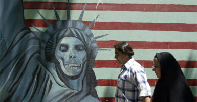 TEHRAN, IRAN: An Iranian couple walk past an anti-US mural painting outside the former United States' embassy in Tehran, 07 June 2005. Iranian voters are more accustomed to hearing their politicians chant "Death to America" -- but ahead of next week's presidential election the issue of relations with the US has been turned on its head. It is an ironic shift for the Islamic republic, founded on the dogma of resisting "Zionist-American conspiracies" and priding itself on standing up to the "Great Satan". AFP PHOTO/ATTA KENARE (Photo credit should read ATTA KENARE/AFP via Getty Images)