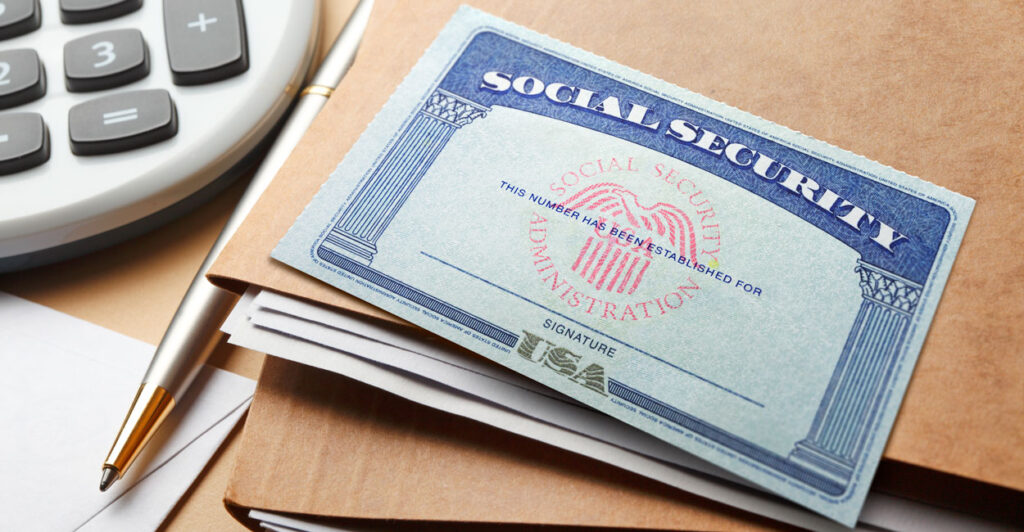 A Social Security card lays atop brown folders next to a calculator.
