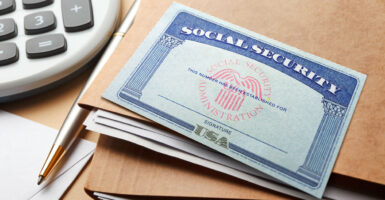 A Social Security card lays atop brown folders next to a calculator.