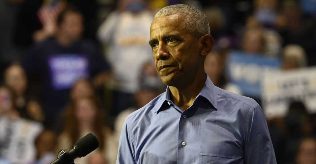 Barack Obama in a blue shirt looking stern.