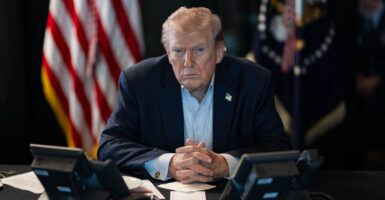 A stern and intense President Trump sits hand folded staring into camera.