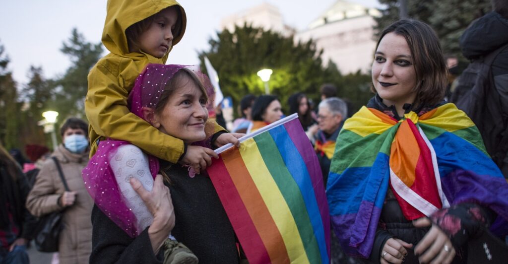 One adult woman and two female children holding rainbow flags.