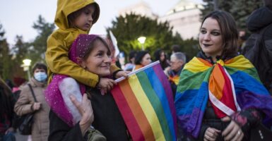 One adult woman and two female children holding rainbow flags.
