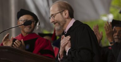 Man in academic robes with his hands against his heart standing at a podium.