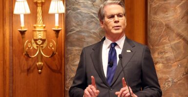 Scott Bessent speaking at a podium with his fingers raised.