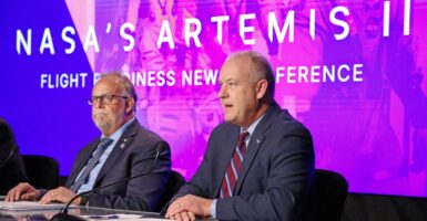 Two men sitting at a table in front of the words "Artemis II."