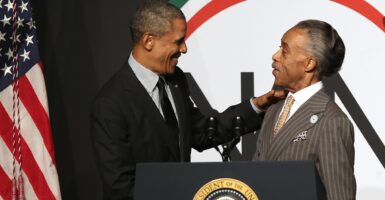 President Barack Obama greets Rev. Al Sharpton on a podium.