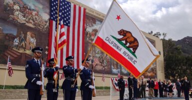 Uniformed men at a Veterans Day observance with a California flag.